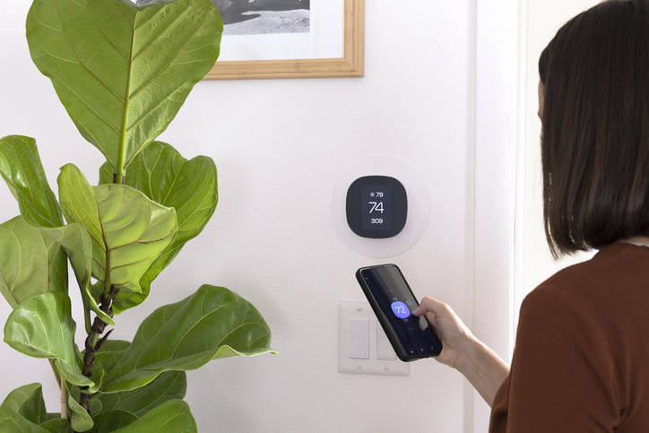 A woman using a smartphone to adjust the room temperature